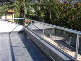 Balcony in the sun with silver handrail and palm trees in the garden