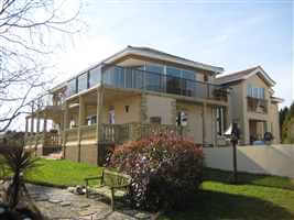 Large house with Bronze handrail balcony with grey tinted glass, surrounded by beautiful views