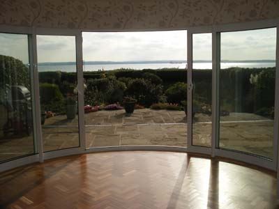 Open white Curved Glass Doors looking onto a beautiful garden with sea views