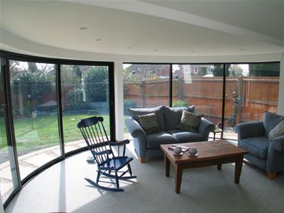 inside view of a Curved Glass Patio looking out onto a small garden from a lounge with  rocking chair